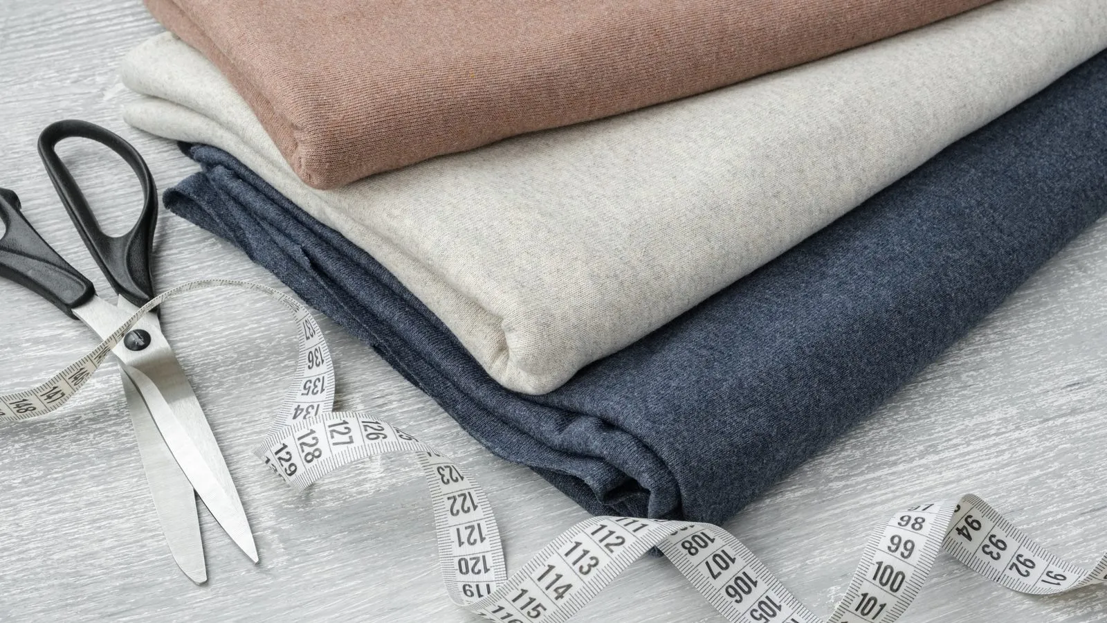 Folded fabrics with a tape measure and scissors, ready for a made-to-measure project
