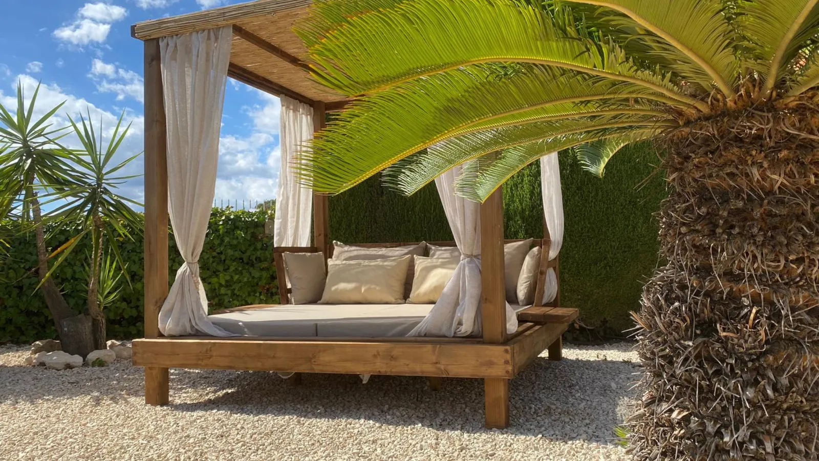 Wooden daybed with handmade cushions under a palm on a Marina Alta terrace